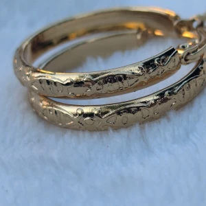 Guldiga örhängen med mönster i rostfritt stål  - Säljer ett par snygga guldiga örhängen med ett unikt mönster. De är i form av ringar och har en elegant och tidlös design.Nya och aldrig använt 