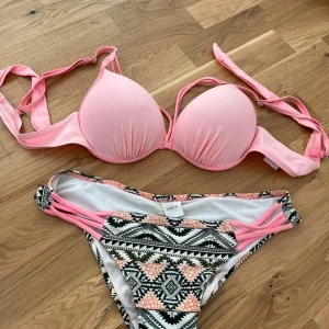 Rosa bikini med mönstrade detaljer - Säljer en superfin rosa bikini med vadderad överdel och knytband. Underdelen har ett snyggt etniskt mönster i svart och rosa med vita inslag. Perfekt för sommarens stranddagar! 💖