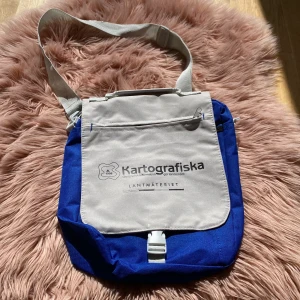 Blå och vit axelväska från Lantmäteriet - Säljer en praktisk och snygg axelväska i blått och vitt från Lantmäteriet. Väskan har en justerbar axelrem och en framficka med dragkedja. Perfekt för vardagsbruk eller utflykter! Helt ny fick på jobbresa