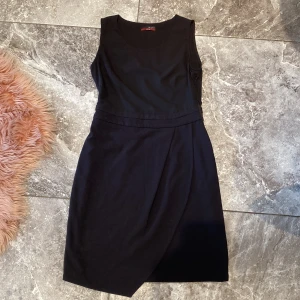 Svart ärmlös klänning - Snygg och elegant svart ärmlös klänning med en omlott-design. Perfekt för både fest och mer formella tillfällen. Klänningen har en stilren och tidlös look.