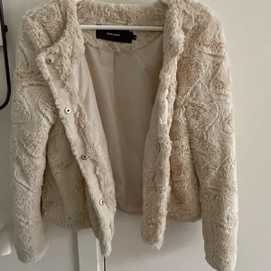 Jacka i pälsimitation från Vero Moda - Kort beige jacka i pälsimitation från vero Moda. Jackan försluts med knappar. Helt ny aldrig använd 