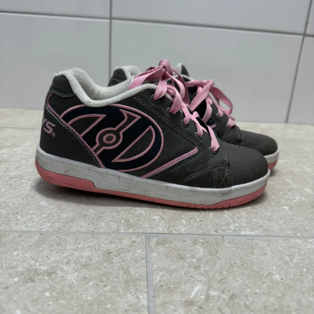 Säljer ett par coola Heelys i svart och rosa. Skorna har en unik design med hjul i sulan för att rulla fram. De är i bra skick med rosa snörning och detaljer. Perfekta för den som vill glida runt med stil!. Skor.