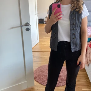 Grå väst från Vila - Säljer en snygg grå väst från Vila. Den har en cool militärinspirerad stil med dubbla rader av knappar framtill. Perfekt för att ge din outfit en edgy touch. Västen är ärmlös och har en normal passform. Passar bra till både vardag och fest!