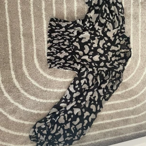 Skönnn tröja - Tröjan har ett svart mönster med ljusgrå fläckar, lite som ett oregelbundet kamouflagemönster. Den har puffiga ärmar och ett smockat parti vid midjan som gör att den sitter åt där. Materialet är lätt och luftigt.😍😍❤️