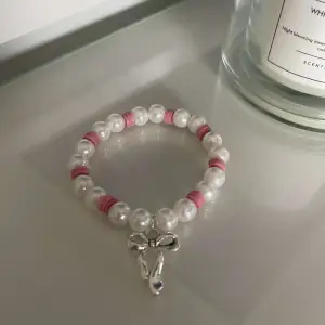 Säljer ett supergulligt armband med vita pärlor och rosa detaljer. Armbandet har en söt liten rosett som hänge, vilket ger det en extra charmig touch. Perfekt för att piffa upp vilken outfit som helst!