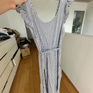 Klänning  - Letar du efter det ultimata statement-plagget för ditt nästa evenemang? Sök inte längre! Vår ärmlösa, rygglösa festklänning utstrålar elegans och sofistikering. Med sin eleganta design och smickrande silhuett är denna klänning perfekt för att göra en