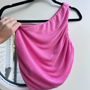 Rosa one-shoulder topp - En stretchig one-shoulder blus med dubbelt tyg. Kan därför med lätthet bäras utan bh! Likadan på framsidan och baksidan, man kan alltså bära den på antingen höger eller vänster axel.  Passar till S/M 🥰  (ALDRIG ANVÄND)  Längd: 37 cm Byst: 78 cm