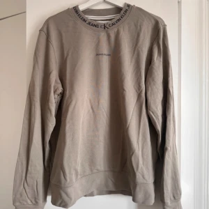Calvin Klein sweatshirt  - Grön/khaki sweatshirt från Calvin Klein. Svart tryck på bröstet och svart text från halsen. Tröjan är i väldigt fint skick då den används kanske 2 gånger. 