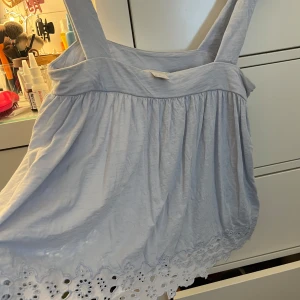 Ljusblå ärmlös topp med broderad kant - Säljer en söt ljusblå ärmlös topp i bomull. Den har breda axelband och en vacker broderad kant längst ner. Perfekt för sommardagar eller en avslappnad utflykt. Toppen är i storlek XS och i bra skick.