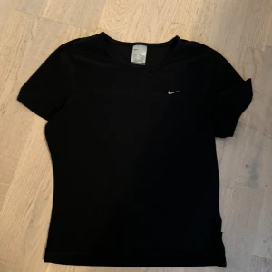 Svart t-shirt från Nike - Säljer en svart t-shirt från Nike i storlek M. Den har en enkel och stilren design med korta ärmar och en liten Nike-logga på bröstet. Perfekt för träning eller vardagsbruk. Materialet är mjukt och bekvämt, vilket gör den idealisk för aktiva dagar.