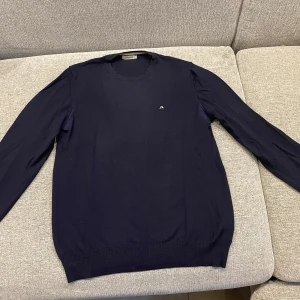 Mörkblå merinoulltröja från J.Lindeberg - Säljer en stilren och bekväm mörkblå tröja från J.Lindeberg i 100% merinoull. Perfekt för kyliga dagar med sin mjuka och värmande känsla. Tröjan har långa ärmar och en diskret logga på bröstet. Passar både till vardags och lite finare tillfällen.