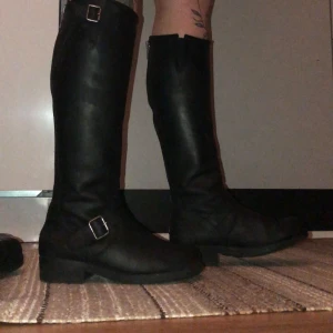 Höga Johnny bulls  - Säljer ett par svarta höga stövlar i skinn med snygga spännen och dragkedja bak. Perfekta för höst och vinter, de ger en cool look och är superbekväma. Passar både till vardags och fest. Använda men i mycket bra skick!