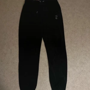 Svarta mjukisbyxor från Juicy Couture - Säljer ett par svarta mjukisbyxor från Juicy Couture i storlek S. Byxorna har en hög midja med snörning och texten 'Juicy' i glittriga bokstäver på baksidan. Perfekta för en avslappnad och stilren look. 🖤