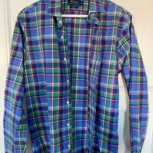 Rutig skjorta från Polo Ralph Lauren - Säljer en snygg rutig skjorta från Polo Ralph Lauren i storlek S. Skjortan har ett klassiskt rutmönster i blått, grönt och rött med långa ärmar och knappar framtill. Perfekt för både vardag och fest! 💙💚❤️