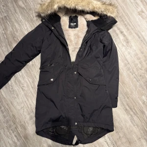 Svart parkajacka från 8848 Altitude - Säljer en svart parkajacka från 8848 Altitude i storlek 36. Jackan har en mysig fuskpälsfodrad huva och flera praktiska fickor med både dragkedja och knappar. Perfekt för kalla vinterdagar! ❄️vatten o vin tät. 