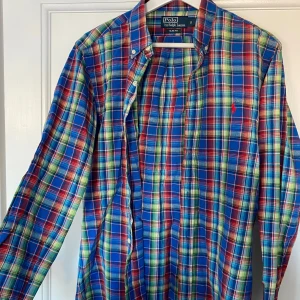 Rutig skjorta från Polo Ralph Lauren - Säljer en snygg rutig skjorta från Polo Ralph Lauren i slim fit. Skjortan har ett färgglatt mönster i blått, rött och grönt med knappar framtill. Perfekt för både vardag och fest! 🕺