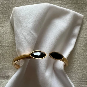 Guldarmband med svarta stenar från Dyrberg Kern - Snyggt roséguldarmband med två svarta, ovala stenar i ändarna. Armbandet har en elegant och stilren design, perfekt för både vardag och fest. Det är i mycket bra skick och har en praktisk låsmekanism som gör det enkelt att ta på och av.