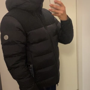 Svart dunjacka från Sail Racing - Säljer en svart pufferjacka från Sail Racing i nyskick. Jackan har en huva och dragkedja framtill. Den är både varm och bekväm, håller vintern ut utan problem. Perfekt för kalla vinterdagar! Den är i absolut nyskick, ej använd, endast testad. Nypris=6000kr säljer för 3900kr då jag vill bli av med den. Ni hittar ingen bättre och snyggare vinterjacka för bättre pris 😉