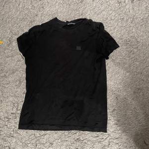 Säljer en stilren svart t-shirt från Acne Studios i bra skick. Den är kortärmad och har en liten fyrkantig detalj på bröstet. Perfekt för vardagsbruk eller att klä upp med accessoarer. Passar till alla säsonger! Priset är inte hugget i sten