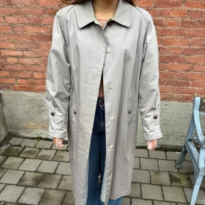 Beige trenchcoat - Säljer en stilren beige trenchcoat i bra skick. Den har långa ärmar och knappar framtill. Perfekt för höst och vår, och ger en klassisk look till vilken outfit som helst. Passar både till vardags och lite finare tillfällen.