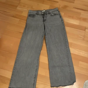 Grå jeans med rå kant - Säljer ett par grå jeans från Perfect Jeans i storlek 34. De har en cool rå kant nertill och en klassisk femficksdesign. Perfekta för en avslappnad look med en loose passform. Passar bra till både vardag och fest! Lågmidjade!