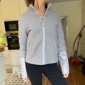 Grå fleecejacka i ull med dragkedja - Säljer en supermysig grå fleecejacka med dragkedja och hög krage. Jackan har en cool textur och långa ärmar med en unik design där det ser ut som en extra lager vid ärmsluten. Perfekt för kyliga dagar! 