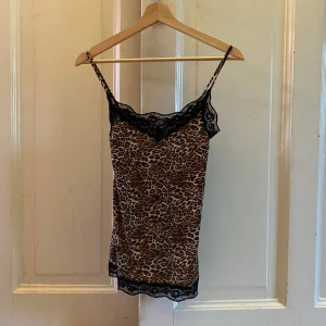 Leopardmönstrad linne med spetsdetaljer - Säljer ett snyggt leopardmönstrat linne med svarta spetsdetaljer vid halsringningen och nederkanten. Perfekt för en utekväll eller ev vardags outfit med jeans. Linnet har smala axelband och är i mycket bra skick.