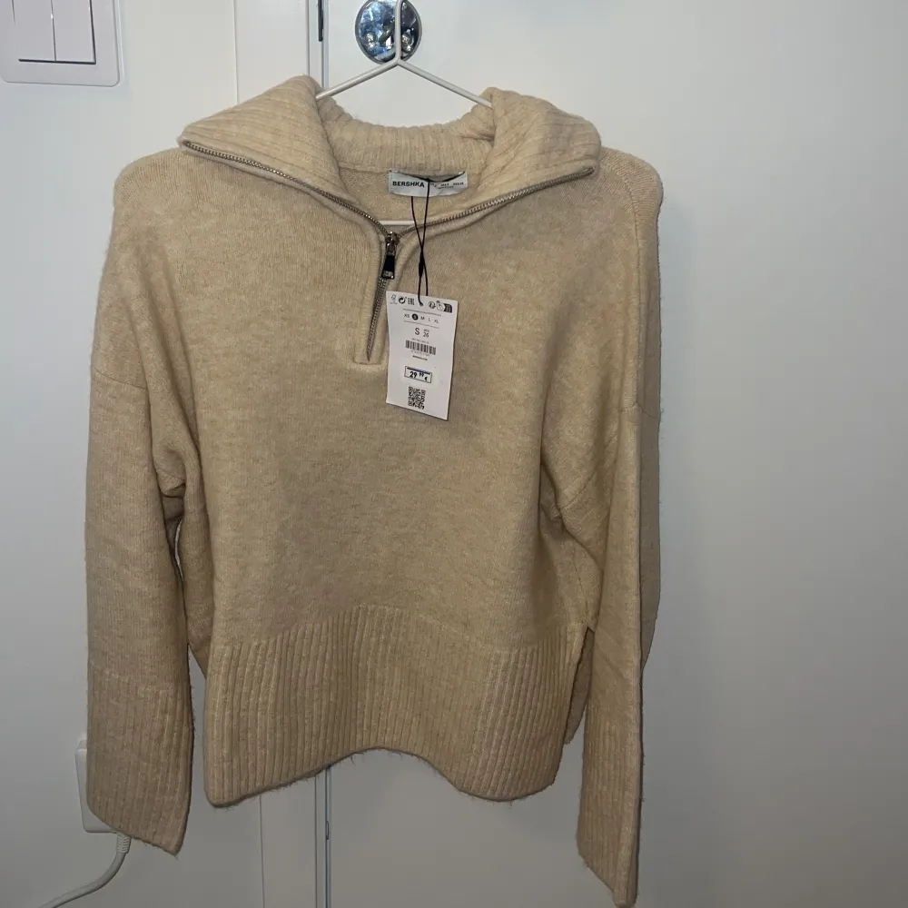 Säljer en supermysig beige stickad tröja från Bershka. Den har en dragkedja vid halsen och ribbade detaljer vid ärmslut och nederkant. Perfekt för kyliga dagar och passar både till vardags och lite finare tillfällen. Helt ny med tag kvar! 🧥✨. Tröjor & Koftor.