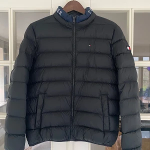 Svart pufferjacka från Tommy Hilfiger - Säljer en snygg svart pufferjacka från Tommy Hilfiger. Jackan har en dragkedja framtill och är dekorerad med det klassiska Hilfiger-logotypen på ärmen, bröstet och kragen. Jackan är nyskick! Storlek 176 men passar även XS/S.