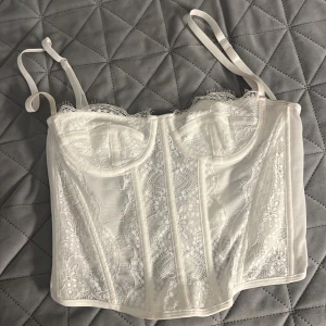Vit spetskorsett - Säljer en superfin vit korsett med spetsdetaljer. Den har justerbara axelband och en hakknäppning bak för perfekt passform. Perfekt för fest eller en speciell kväll. Helt ny bara använt 1 gång 