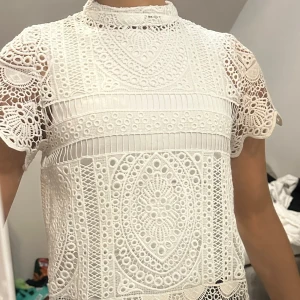Vit spetsblus från Gina Tricot - Säljer en superfin vit spetsblus från Gina Tricot i storlek 34. Blusen har korta ärmar och ett detaljerat spetsmönster. Perfekt för både vardag och fest! Den har en dragkedja i ryggen för enkel påklädning.