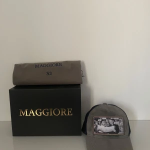 Maggiore keps - Snygg grå keps från Maggiore med marinblått nät på baksidan och en cool bild framtill. Perfekt för en avslappnad stil eller en dag ute i solen. Kepsen kommer i en stilren förpackning och är i nytt skick. Tveka inte att höra av dig om du har frågor eller funderingar😁