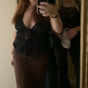 Svart topp med knytning - Snygg svart topp med knytning framtill och djup v-ringning. Perfekt för en utekväll eller fest. Toppen har en figurnära passform och är tillverkad i ett mjukt material som sitter bekvämt hela kvällen.