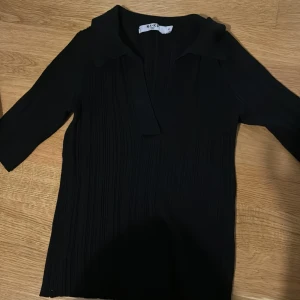 Svart topp från NA-KD - Snygg svart bastopp från NA-KD i storlek XS. Den har en v-ringad design och är gjord i ett ribbat material som ger en elegant look. Perfekt för både vardag och festliga tillfällen!