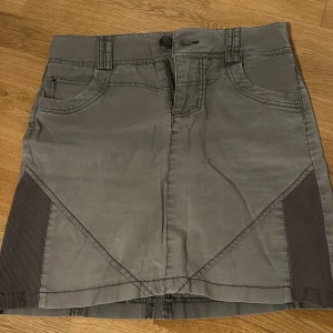 Grågrön kjol från Cream - Säljer en snygg grå/khaki-grön kjol från Cream i storlek 36. Kjolen har en dragkedja fram och en knappdetalj i midjan. Den är perfekt för både vardag och fest med sin stilrena design. Passar bra till höst och vår. 🖤