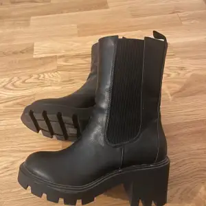 Snygga svarta boots från Bianco i storlek 38. De har en chunky sula och resår på sidorna för enkel påtagning. Perfekta för höst och vinter med en stilren look som passar till allt. Oanvända!