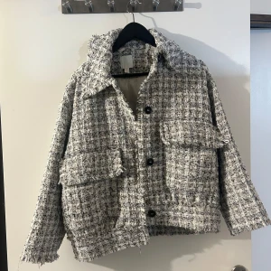 Tweedjacka från H&M - Säljer en snygg tweedjacka från H&M i svart och vit, har olika färg detaljer även som man kan se om man zoomar in på bilden. Jackan har en klassisk krage och stora fickor framtill. Perfekt för höst och vår, med en chic och tidlös stil. Den är i mycket bra skick och passar perfekt för både vardag och fest. Säljs inte länge i butik! 