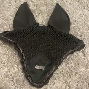 Grå hästhuva från Equestrian Stockholm - Snygg och stilren svart hästhuva från Equestrian Stockholm. Den är stickad med fina detaljer och har en elegant kant. Perfekt för ridning och att hålla insekter borta. Passar bra för både träning och tävling. Storlek ponny! Sparsamt använd och i fint skick🩶🩶