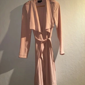 Gammalrosa kappa från Object - Säljer en elegant gammalrosa kappa  från Object i storlek XS. Kappan har långa ärmar och ett knytbälte i midjan för en smickrande passform. Perfekt för både vardag och festliga tillfällen. 💫