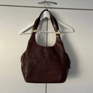 Brun skinnväska - Säljer en snygg brun skinnväska ibra skick. Den har guldfärgade detaljer. Bilden är lånad från förra säljaren.