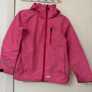 Rosa vindjacka från Quechua - Säljer en snygg rosa vindjacka/höst från Quechua i mycket bra skick (barnjacka). Jackan har en dragkedja framtill och en praktisk bröstficka med dragkedja. 