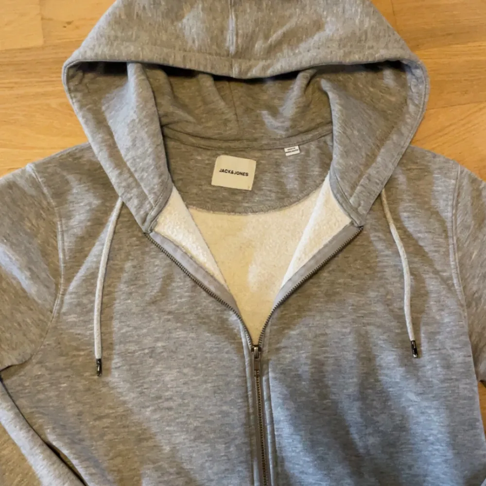 Säljer en grå hoodie från Jack & Jones i mycket bra skick. Den har en dragkedja framtill och en justerbar huva med snören. Perfekt för höst och vår, och den är superbekväm att ha på sig. Passar till både chill och vardagsoutfits! Storlek L men passar mig som brukar ha M bra!. Tröjor & Koftor.