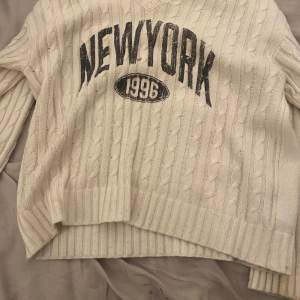 Säljer en supermysig vit stickad tröja med texten 'NEW YORK 1996' i svart på framsidan. Tröjan har en avslappnad passform och långa ärmar med ribbade muddar. Perfekt för kyliga dagar när du vill vara både bekväm och stilren. 🗽