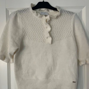 Vit stickad tröja från Holly & White  - Säljer en superfin vit stickad tröja från Holly & White. Den har en söt volangkrage och knappar framtill. Tröjan är kortärmad och perfekt för vår och sommar. Den är i mycket bra skick och passar både till vardags och fest. Perfekt att matcha med jeans eller kjol!