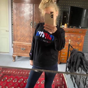 Svart långärmad tröja från Trapstar - Säljer en svart långärmad tröja från Trapstar med färgglatt broderi i blått, rött och vitt på bröstet. Texten 'IT'S A SECRET' ger en mystisk touch. Perfekt för höst och vinter, och den är i mycket bra skick. Passar både till vardags och chill.