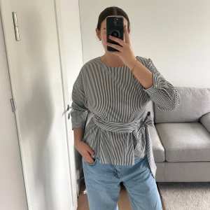 Fin unik blus med rosett - Väldigt fin unik blus, två band sitter fast i sidan (bild 3) som knyts runt midjan för att skapa rosetten. Blusen är randig i vitt och blått