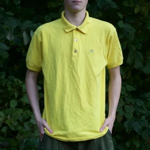 Gul pikétröja - Säljer en snygg gul pikétröja i bomull. Den har en klassisk krage med två knappar och korta ärmar. Perfekt för sommardagar eller en avslappnad vårlook. Tröjan är i bra skick och passar både till vardags och lite finare tillfällen.