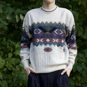 Mönstrad stickad tröja i beige och färger - Säljer en supermysig stickad tröja med ett coolt geometriskt mönster i beige, blått, lila och grönt. Perfekt för höst och vinter! Tröjan har långa ärmar och ribbade muddar, vilket gör den både varm och stilren. Passar perfekt för en chill dag ute i naturen eller en mysig hemmakväll. 🧶✨