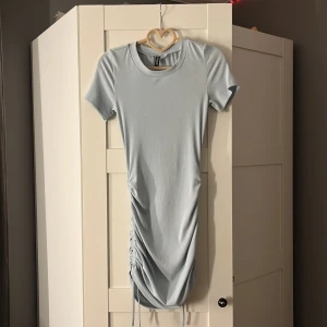 Ljusblå klänning från H&M Divided - Säljer en superfin ljusblå klänning från H&M Divided i storlek XS. Den är kortärmad och har en snygg snörning på sidan som ger en rynkad effekt. Perfekt för sommaren eller en utekväll! Materialet är mjukt och stretchigt för en bekväm passform. 🩵