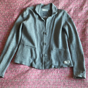 Grå kofta / stickad kavaj från Odd Molly storlek 2 - Säljer en snygg grå kofta från Odd Molly i storlek 2. Den har långa ärmar och knappar framtill. Perfekt för höst och vår, med en stilren design och broderad detalj på ryggen. Passar både till vardags och lite finare tillfällen. En klenod i fint skick men sällan använd